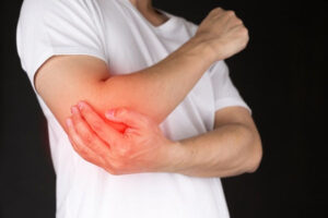 A man in a white shirt holding his right elbow that is highlighted in red to show pain due to overuse.