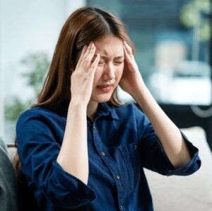 A young Asian woman holding her head in pain.